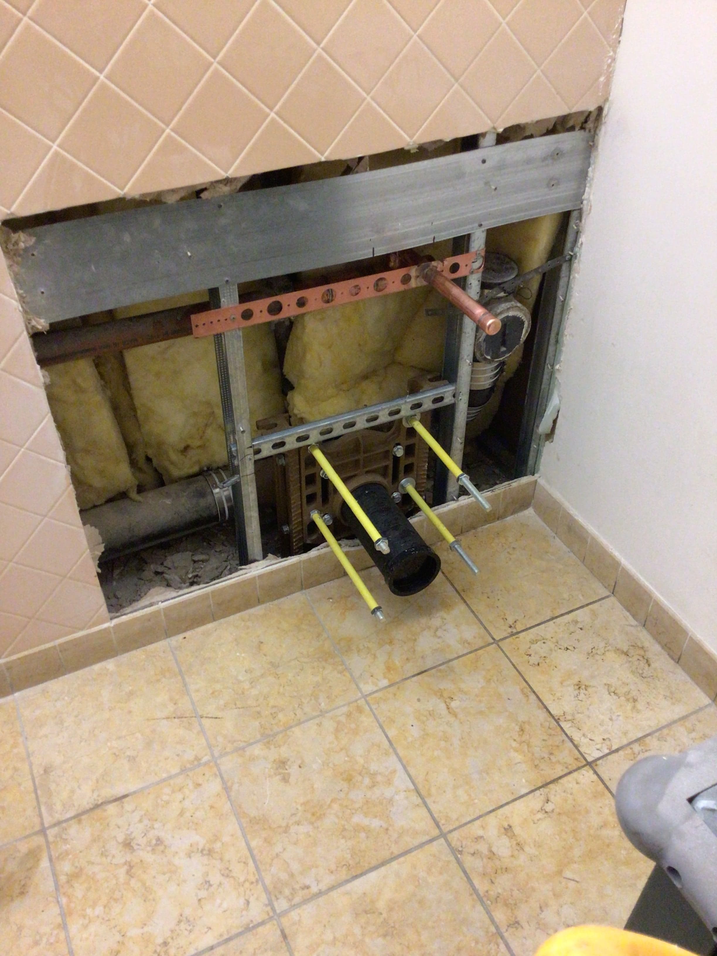 Wall-hung toilet carrier rough-in: 4-inch waste line with test plug, copper supply stub-out, and Unistrut bracing behind tile.