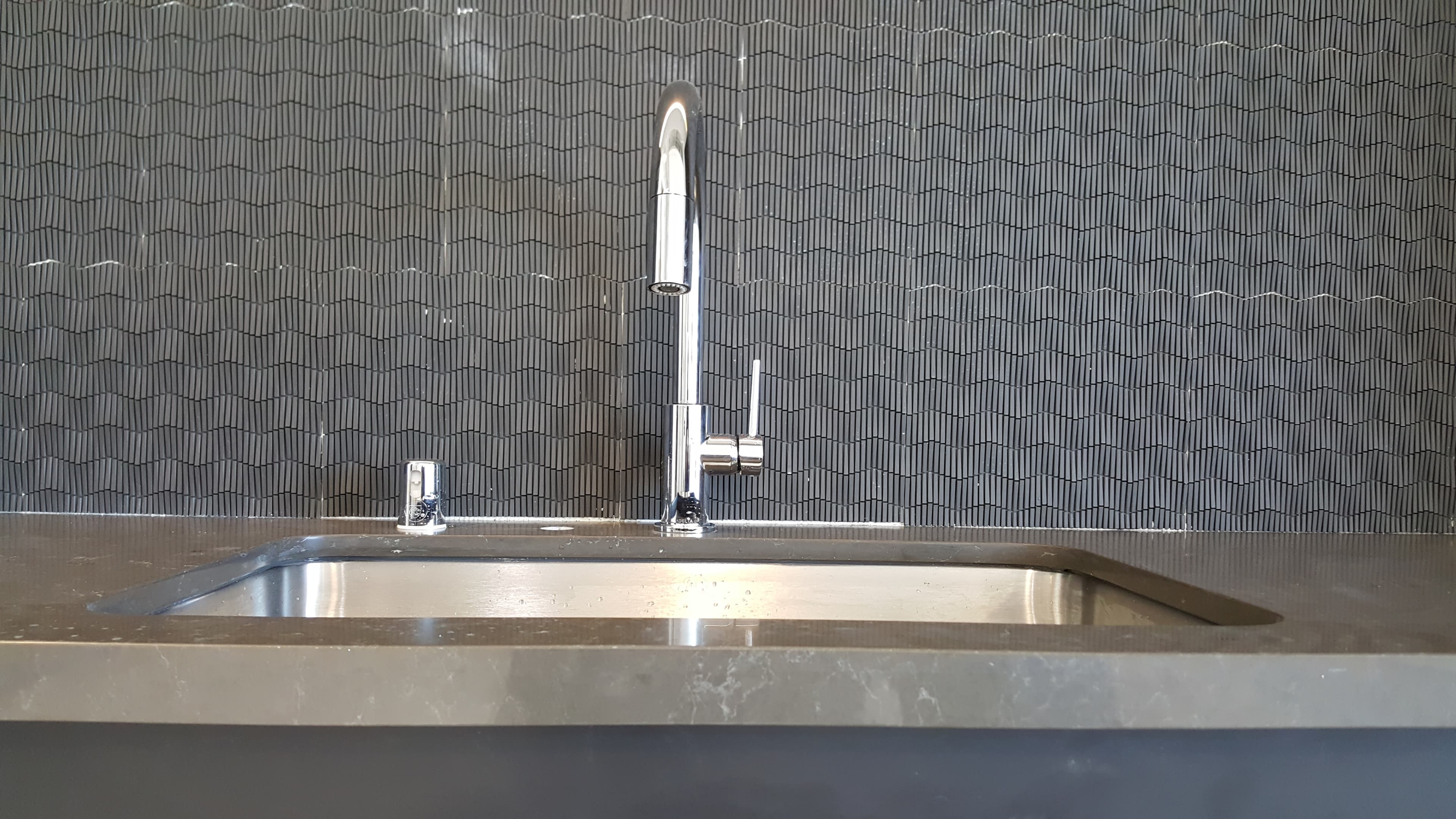 Modern kitchen sink and pull-down faucet with clean backsplash finish.