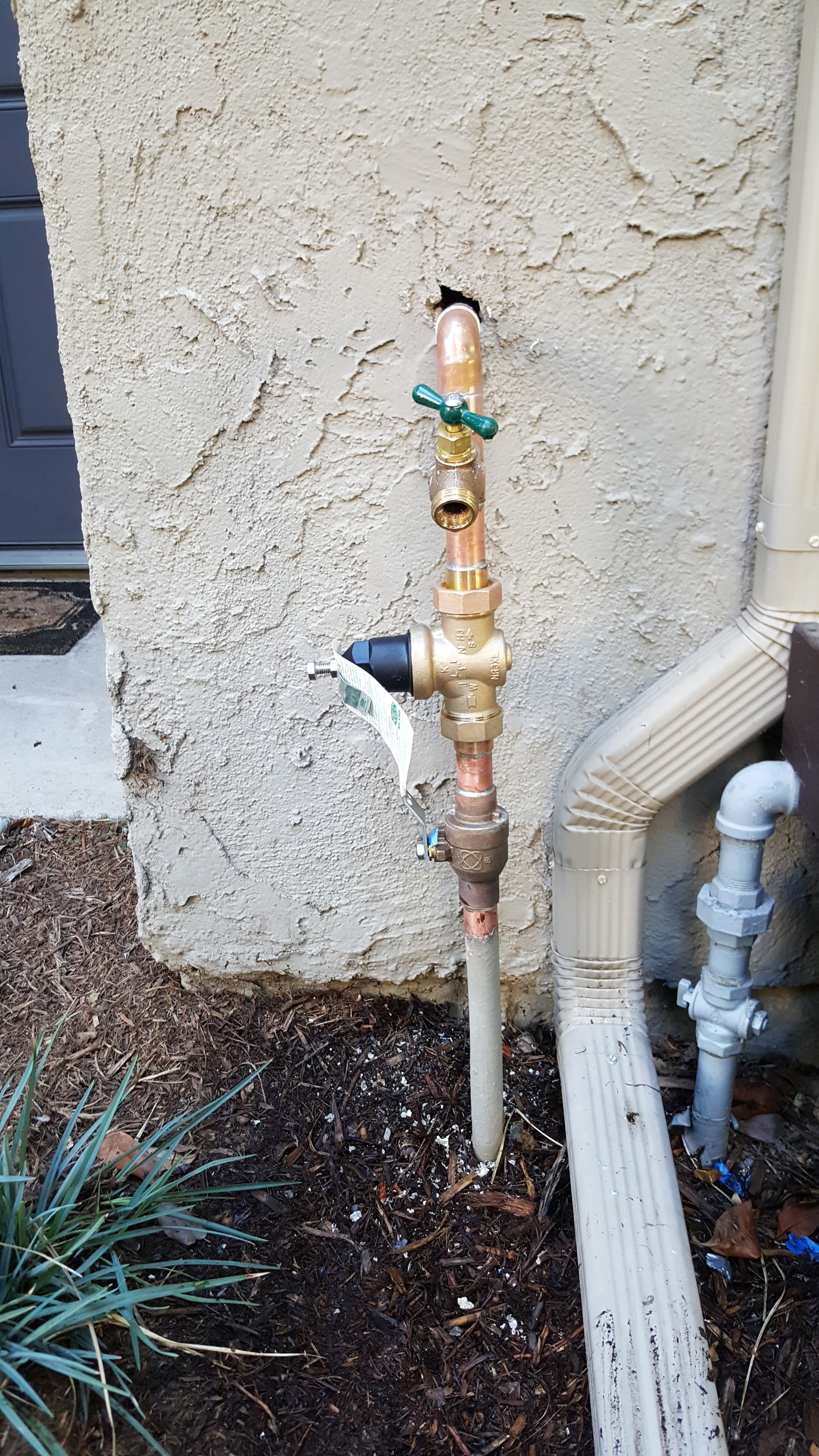 Exterior main water line with pressure regulator (PRV) and hose bib on copper riser.